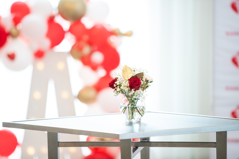 Red rose floral centerpiece with red and white balloon arch in the background.